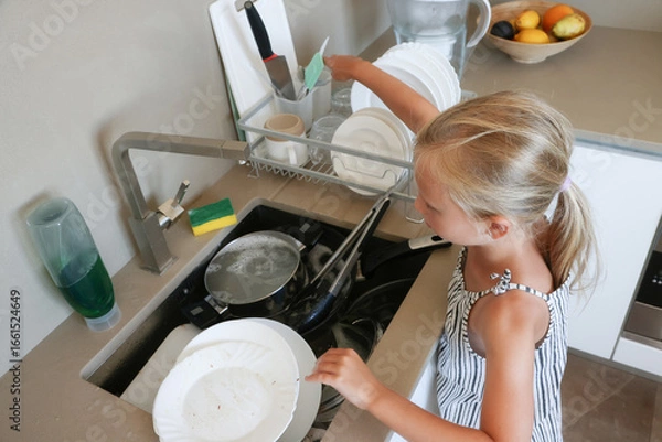 Obraz Girl rinsing fork with sponge under running water at sink