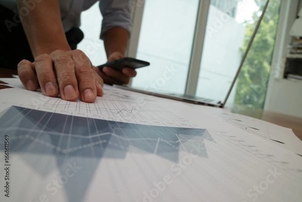 Fototapeta Businessman Analyzing Financial Charts with Laptop and Smartphone