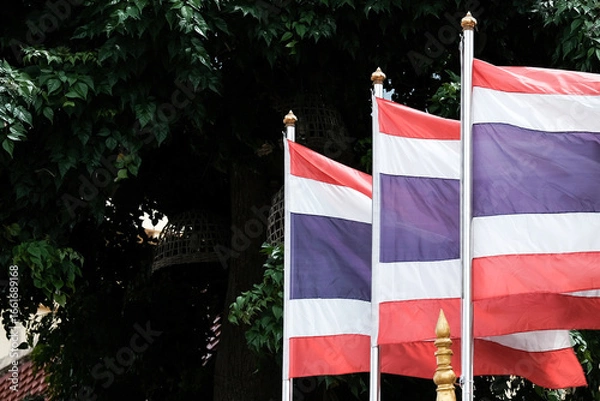 Fototapeta Thai national flag waving in the wind against and leafy green trees, symbolizing pride and unity in Bangkok, Thailand.