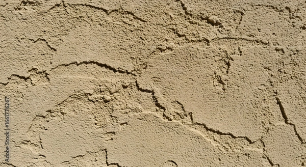 Fototapeta A textured beige surface with deep crevices, illuminated by sunlight, casting shadows to accentuate the roughness and depth of the material, offering a tactile and organic visual experience.