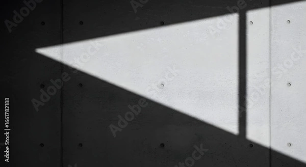 Fototapeta A stark concrete wall is bisected by an acute triangle of light and shadow, casting an austere mood that highlights the material's texture and geometry in minimalist composition for striking effect.