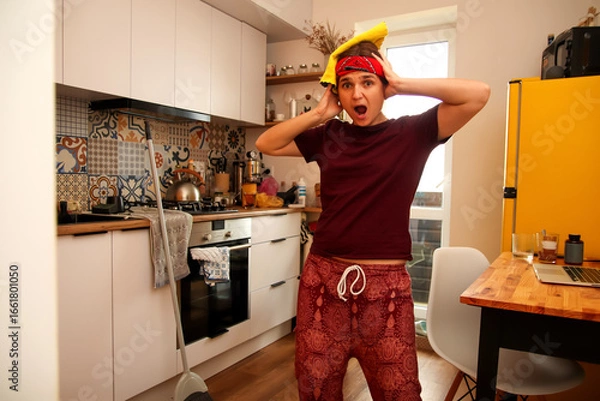 Fototapeta fun image of a Gen Z hipster woman in a dirty kitchen, with a look of surprise or scared on her face.  a yellow rag and a spot of dirt are the focus of the image. Fun clean up concept