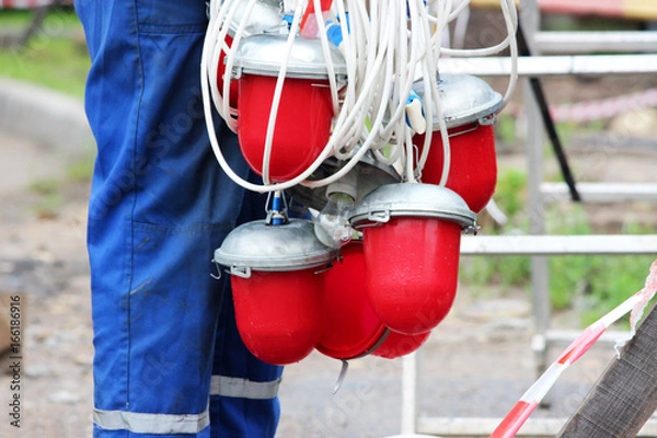 Fototapeta An electrician removes a lot of red warning lights from the fence before dismantling it at the site of the pipeline accident after the work is completed
