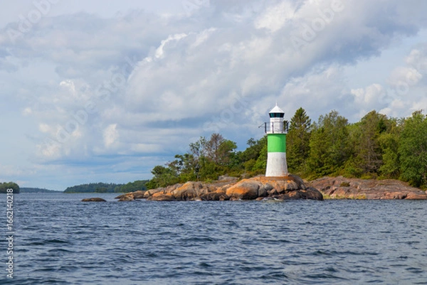 Fototapeta Marine channel marker on coastal rocks with green top, indicating the edge of the channel. Coastal navigation aid in Baltic sea, highlighting safety, marine guidance, and rocky shoreline