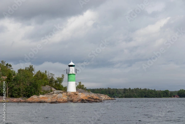 Fototapeta Marine channel marker on coastal rocks with green top, indicating the edge of the channel. Coastal navigation aid in Baltic sea, highlighting safety, marine guidance, and rocky shoreline
