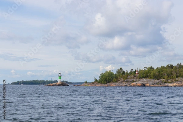 Fototapeta Marine channel marker on coastal rocks with green top, indicating the edge of the channel. Coastal navigation aid in Baltic sea, highlighting safety, marine guidance, and rocky shoreline