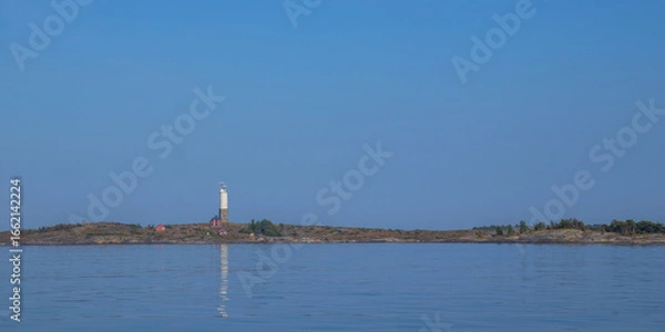 Fototapeta Small lighthouse with adjacent house on rocky islet in the Baltic Sea. Coastal scene in Finland with traditional maritime architecture, peaceful waters, and northern light