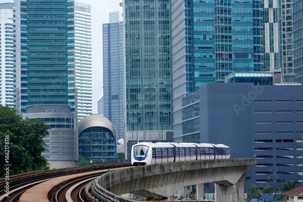 Fototapeta A commuter train is traveling on a concrete elevated track. Background includes modern skyscrapers in Kuala Lumpur, Malaysia. Overcast daylight in urban area.