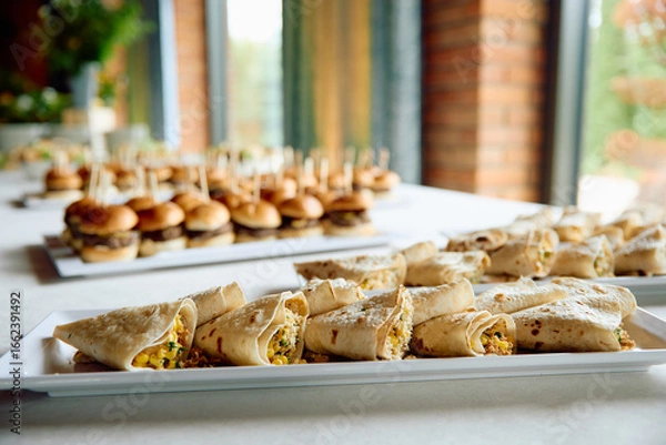 Fototapeta Appetizer wraps and mini burgers on trays at event