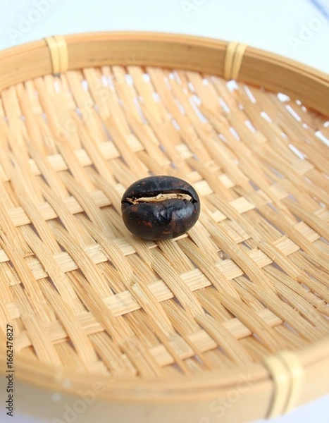 Fototapeta Single dark seed in a woven, light-colored, shallow basket