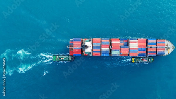 Fototapeta Aerial of cargo ship carrying container running with Tugboat for export cargo from cargo yard port to other ocean concept smart freight shipping ship top view