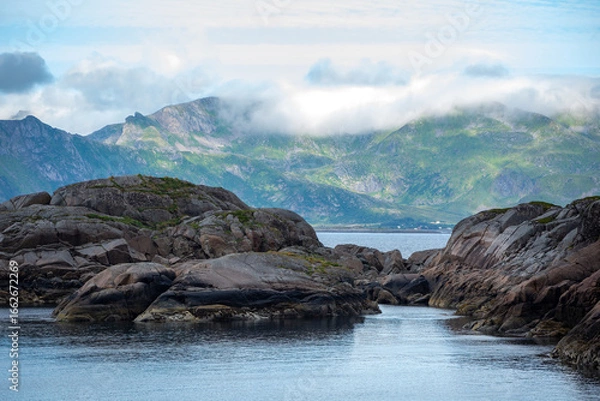 Fototapeta Rocks in shallow water with distant mountains across fjord in Lofoten, in Northern Norway