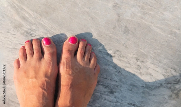 Fototapeta Top view of feet with red nails standing on marble floor capturing a serene summer moment.