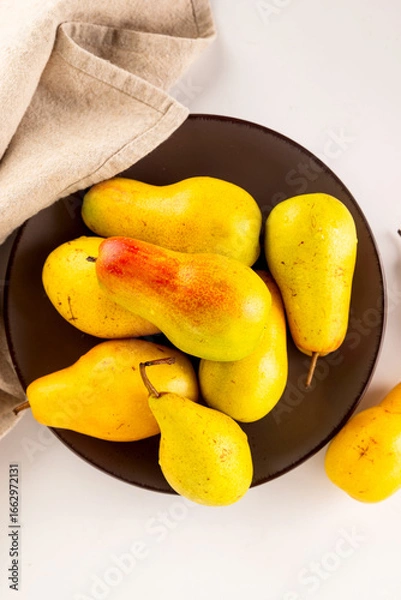 Fototapeta ripe yellow-green pears on plate on a white table.