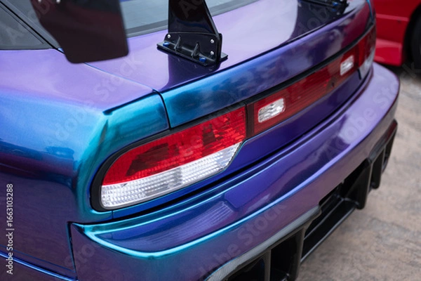 Fototapeta Close-up of the rear taillights and wing mounts on with an iridescent blue and purple vinyl wrap, showcasing its custom JDM tuning