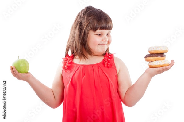 Fototapeta How to teach children to eat healthy food. Girl with food, chooses what to eat donuts or fresh apple, isolated on white background
