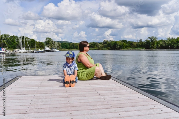 Fototapeta Mum and son enjoying a sunny day by the water on a wooden dock