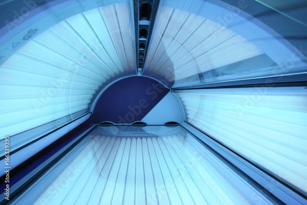 Fototapeta Solarium empty tanning bed in modern beauty salon, view from inside with closed lid and all light bulbs glowing on. Concept of sunbath, beauty lifestyle and healthcare