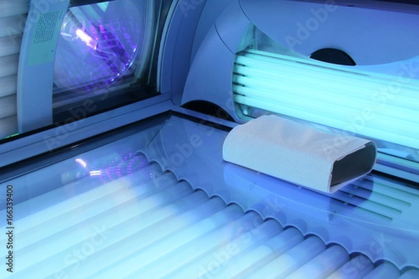 Fototapeta Solarium empty tanning bed in modern beauty salon, view from inside with closed lid and all light bulbs glowing on. Concept of sunbath, beauty lifestyle and healthcare