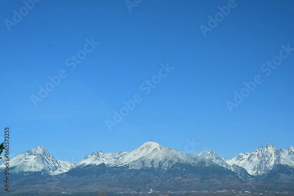 Fototapeta A distant view from the hill of the high peaks of snow-capped mountains High Tatra in spring