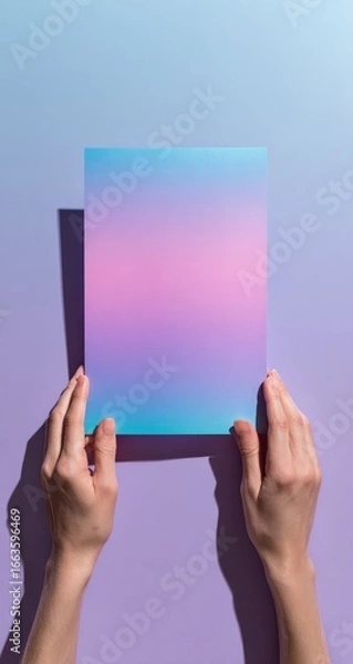 Fototapeta Hands holding a gradient-colored sheet of paper against a pastel background