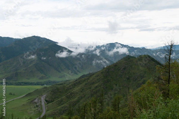 Obraz Mountain valley with lush green grass surrounded by mountain ranges covered with clouds
