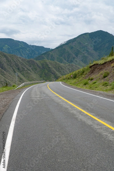 Obraz An asphalt road in a mountainous area stretching into the distance between the slopes of high hills.