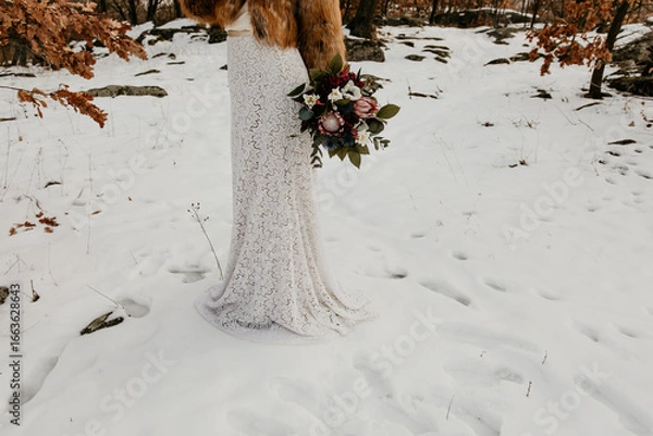 Fototapeta Bride in Lace Dress and Fur Jacket Holding Wedding Bouquet in Snow