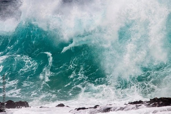 Fototapeta Blue wave crashing on coastal  rocks