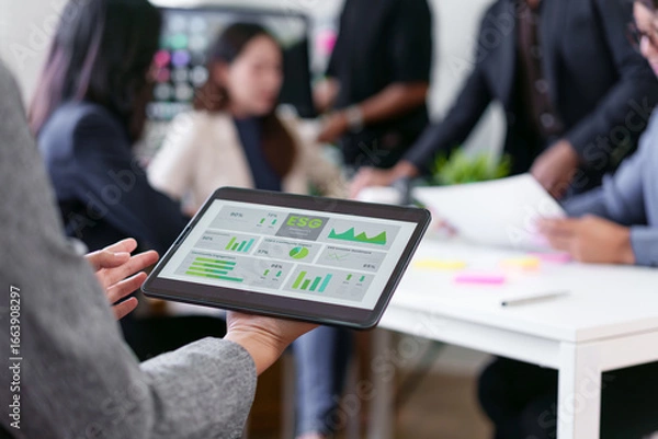 Fototapeta Business team meeting in modern office with tablet displaying ESG data, diverse professionals discussing sustainable strategy, digital technology, teamwork, and financial analysis