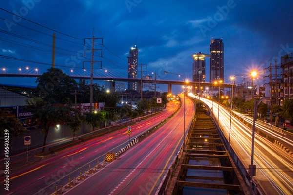 Fototapeta Traffic on city road through modern buildings at twilight in Thailand. Long exposure shot photography by DSLR camera.