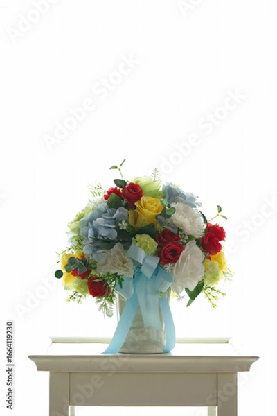 Fototapeta The colorful fake flower vase is located on a white table