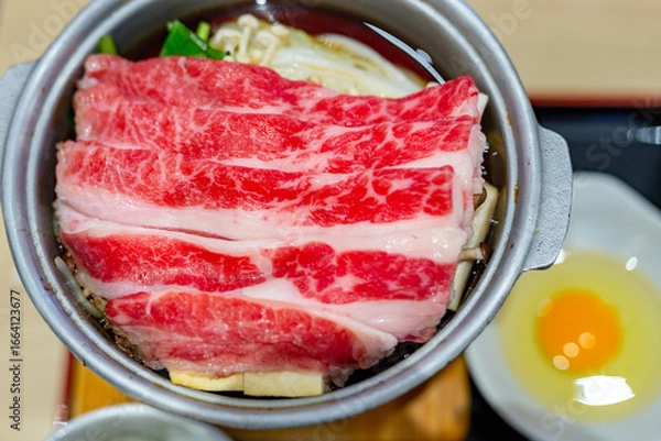 Fototapeta Japanese tasty sukiyaki dish for one person, featuring delicious wagyu beef, fresh vegetables and a raw egg in the restaurant.