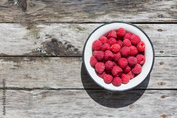 Fototapeta Raspberry in a white plate on an aged wood background. Top view.