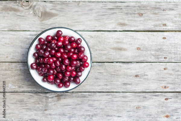 Fototapeta Cherry in a white bowl on a old wooden texture with rasty nails. Top view. Shallow depth of field.