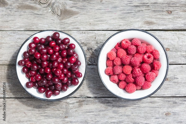 Fototapeta Cherry and raspberry in a bowl on a wooden texture top view. Natural view. Minimalist style.