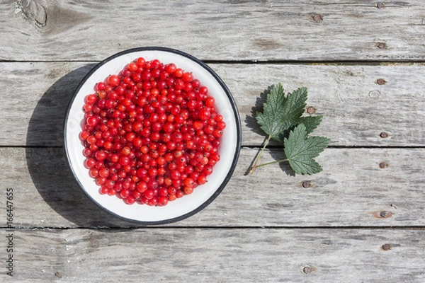 Obraz Red currant in a white bowl on a wooden texture with rusty nails. Top view. Copyspace.