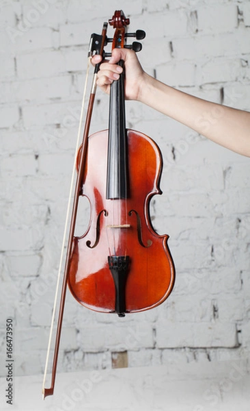 Fototapeta Holding violin with bow under white grand piano with brick wall background
