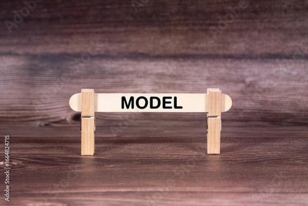 Fototapeta Model symbol. Clothespins gripping a wooden stick against a beautiful Brown Wooden Background . Business and Model concept with copy space