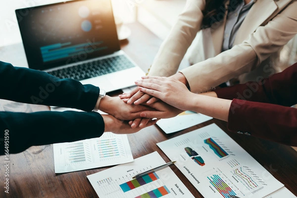 Fototapeta Business people joining hands over financial charts, demonstrating teamwork and collaboration in achieving business goals