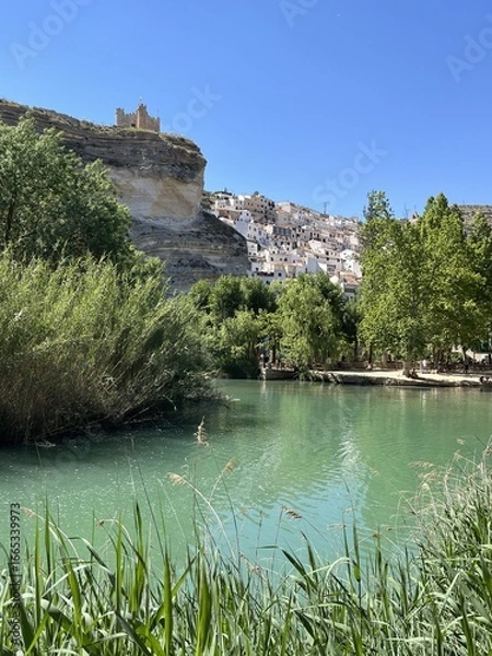 Obraz White rocks and blue river Jucar in Alcala del Jucar with cliffside white houses. Charming Spanish village built into the cliffs of a dramatic canyon, Castilla-La Mancha, Spain
