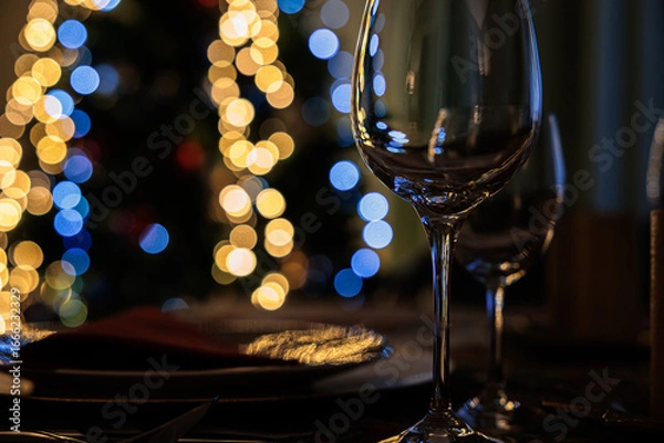 Fototapeta immagine sottoesposta che mostra dei calici vuoti e trasparenti in primo piano, su un tavolo, in una stanza, con luci colorate di un albero di natale, sfuocate sullo sfondo