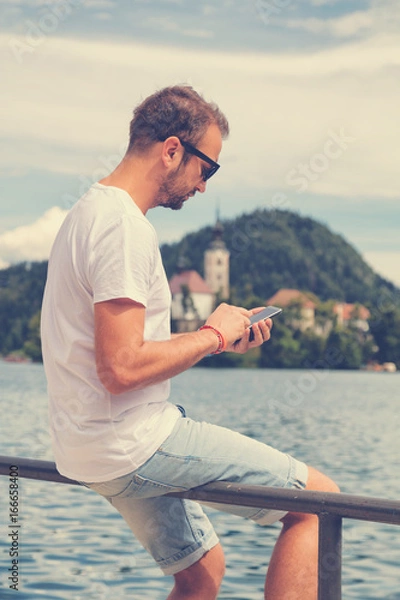 Fototapeta Man sitting on the dock and using a cellphone.