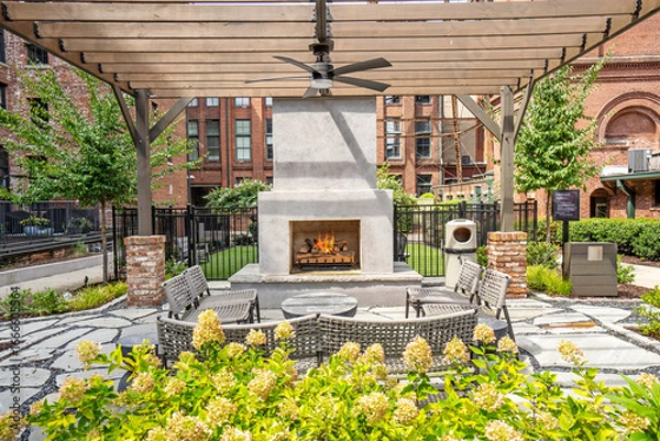 Fototapeta Outdoor lounge area featuring a stone fireplace surrounded by greenery and cozy seating.