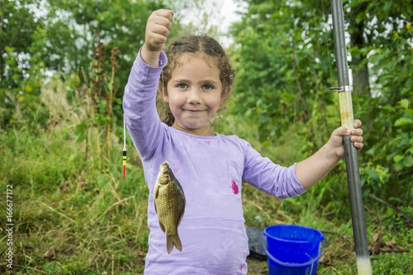 Fototapeta In the summer on a fishing little girl caught a large carp.