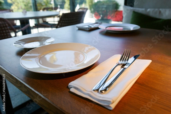 Fototapeta A new clean plate and new clean cutlery on the table in the restaurant.