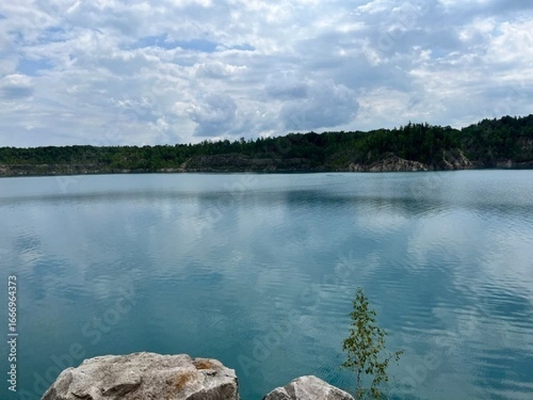 Obraz Scenic lake with calm turquoise water reflecting sky and clouds surrounded by green forest hills