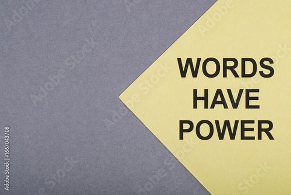 Fototapeta A yellow paper with the phrase WORDS HAVE POWER written in black bold letters is placed on a gray background.