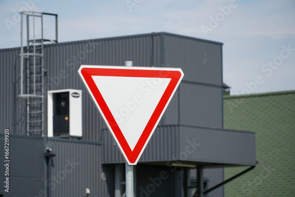 Fototapeta Yield sign stands prominently in front of a modern building during clear weather in an urban area