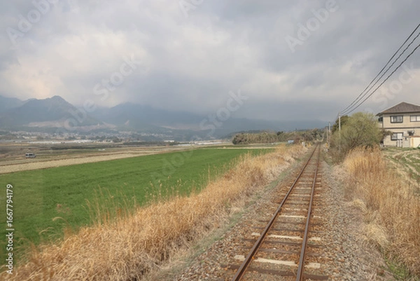 Obraz March 26 2025 Rural Railway Passing Through Scenic Countryside with Fields and Mountains, Japan